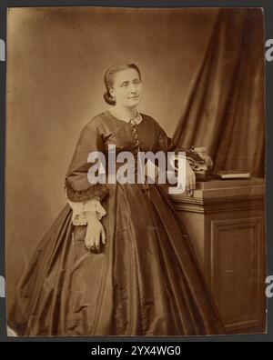 Portrait of a woman, about 1860-1869.  Additional Info: Full length portrait of a woman standing with one arm resting on a short stack of books. The woman is wearing a plain dress with a full skirt and wide sleeves. She has lace undersleeves on and is wearing a long, chain necklace. Stock Photo