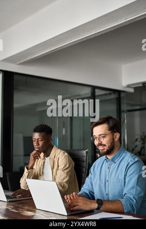 Two busy diverse businessmen employees using laptops working in office. Vertical Stock Photo