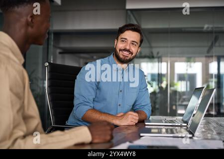Two busy happy business men working on laptops discussing project data at work. Stock Photo