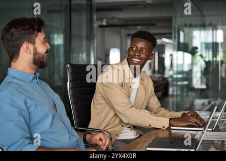 Happy diverse workers team talking at work using computer sharing ideas at work. Stock Photo