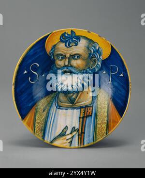 Dish with Saint Peter, about 1500-1520.  Additional Info: This unusually shaped plate with a small base and wide, sloping sides displays a finely painted close-up portrait of Saint Peter. It is one of very few plates painted with a dramatic close-up bust that covers the entire front surface of the work. The plate's rim inventively forms part of the saint's yellow halo so that the two shapes complement each other. To the right and left of Saint Peter's head are the initials <em>SP</em> for San Pietro. The saint is shown as if he were earnestly speaking to the viewer as he points to Stock Photo