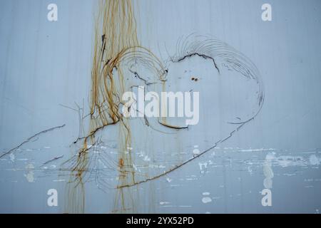 Old wall with a peeled off parts in a shape of heart with a smile. Partly covered by lines of a rust. Harbor of Narvik, Norway. Stock Photo