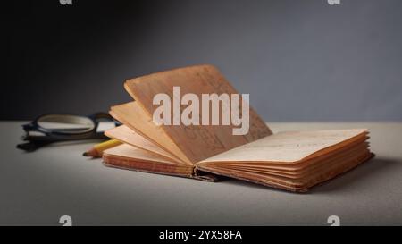 old opened hardback pocket sized diary or journal with glasses and pencil on table top, yellowed pages small brown spots and frayed edges Stock Photo