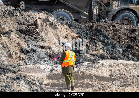 Surveyor carrying out a GPS survey on a construction site, with a dump truck in the background Stock Photo