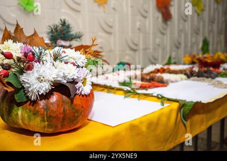 A vibrant table display showcases a pumpkin filled with colorful flowers and autumn leaves. Surrounding the pumpkin are various decorative elements ce Stock Photo
