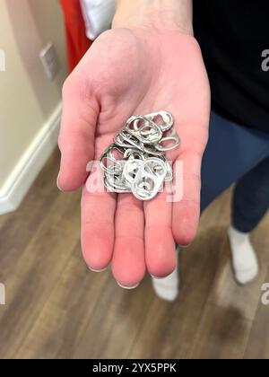 A closeup of a hand holding multiple aluminum can drink tabs that have been removed and collected for recycling to raise money for charity. Stock Photo