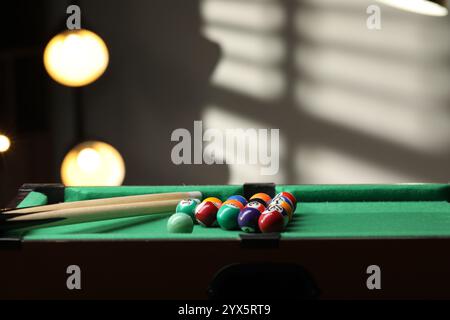 Billiard balls in triangle and cues on green table indoors. Space for text Stock Photo