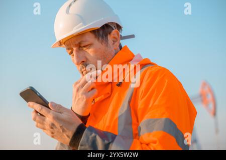 Drilling rig engineer using mobile phone while supervising the process of oil and gas, monitoring rig performance in field, selective focus Stock Photo