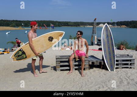 Two male surfers enjoy summer sunshine on a small beach at Wakeport Rhein Main near Raunheim , Hesse , Germany ,Europe Stock Photo