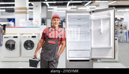 Repairman with a toolbox leaning against a fridge in a shop Stock Photo