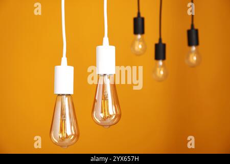 Light bulbs hanging on cords against orange background Stock Photo