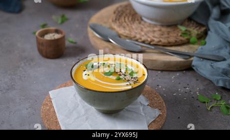 A creamy pumpkin soup garnished with sesame seeds and a swirl of yogurt, served in a bowl on a rustic table. Stock Photo