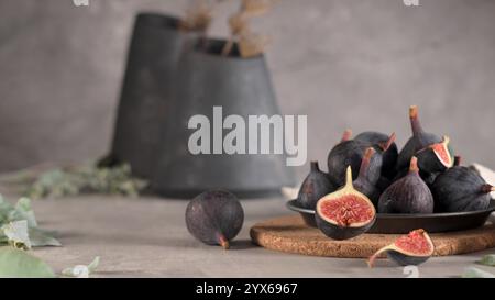 Rustic still life with fresh figs on a cork mat, a black plate, and a blurred background of vases and dried flowers, highlighting the figs' texture an Stock Photo