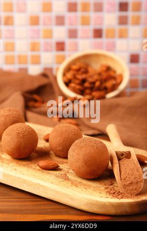 Board with tasty marzipan candies, cocoa powder and almond nuts on wooden table, closeup Stock Photo