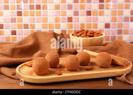 Board with tasty marzipan candies covered with cocoa powder and almond nuts on wooden table Stock Photo