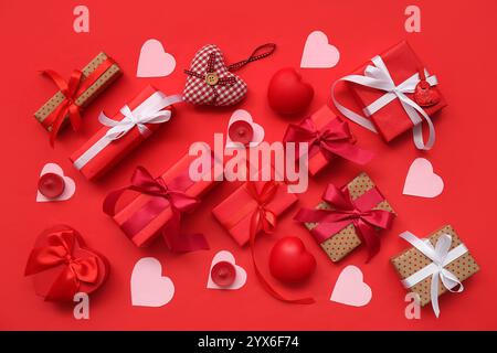 Gift boxes with paper hearts and candles on red background. Valentine's Day celebration Stock Photo