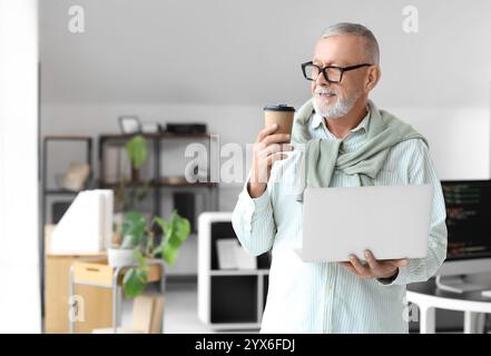 Mature programmer with coffee cup and laptop in office Stock Photo