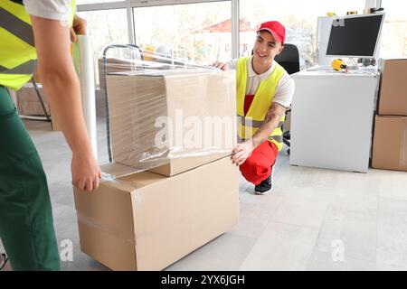 Male loaders wrapping boxes with stretch film in warehouse Stock Photo