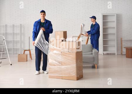 Male worker wrapping cardboard boxes with stretch film in room Stock Photo