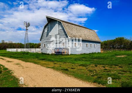 A large, old-fashioned barn sits in a field with a dirt road leading to it. The barn is surrounded by a fence and has a windmill on top. Concept of no Stock Photo