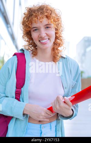 Smiling red-haired student with backpack and books outdoors.Vertical Stock Photo