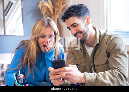 Excited couple sharing a surprising moment while looking at a smartphone Stock Photo