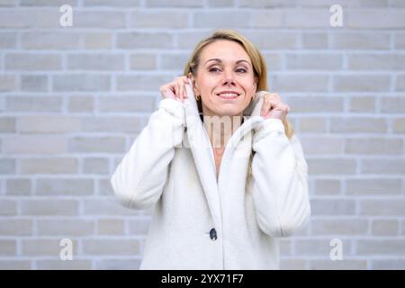 A blonde woman wearing a white coat smiles subtly while holding her collar gently. Stock Photo