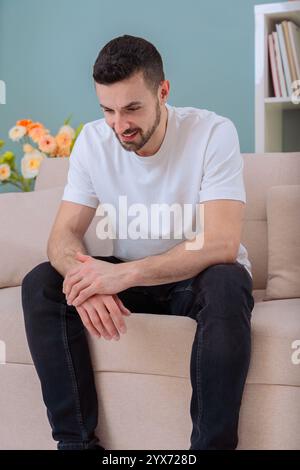 Pensive man sitting on a sofa with thoughtful expression in a cozy room.Vertical Stock Photo