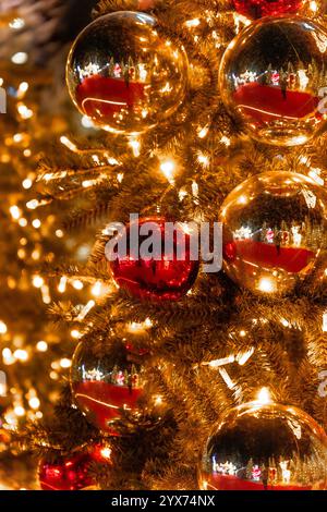 Close-up of warm golden Christmas decorations and lights on a Christmas fir tree decorated with Christmas balls reflecting other Christmas trees and a Stock Photo