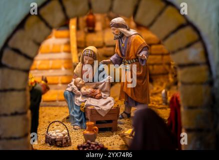 Nativity scene with figures of Mary, Joseph and baby Jesus in a rustic manger with baskets of eggs, fruit and a ceramic jug. Stock Photo