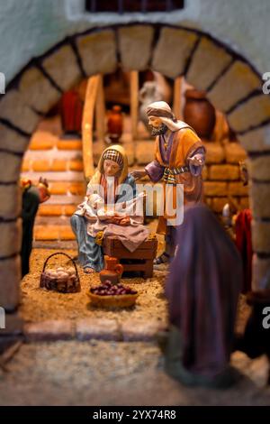 Nativity scene with figures of Mary, Joseph and baby Jesus in a rustic stable with baskets of eggs, fruit and a ceramic jug. Stock Photo