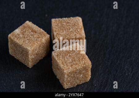 Brown cane sugar cubes on dark stone background, closeup Stock Photo