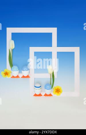 Easter eggs in cute chicken egg cups background border with spring flowers and white frames. Abstract surreal geometric design for holiday season. Stock Photo
