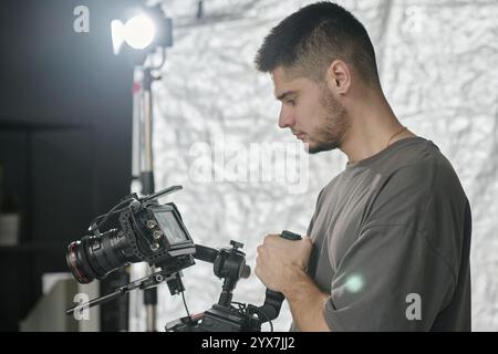 Side view of young adult man holding huge professional camera and looking at display Stock Photo
