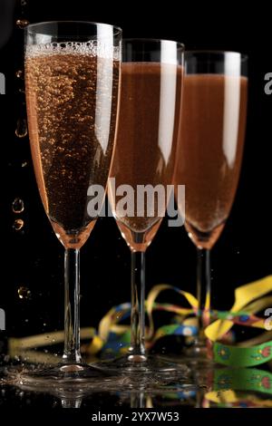 Three champagne glasses on a dark background, liquid bubbling, colourful ribbons next to them Stock Photo
