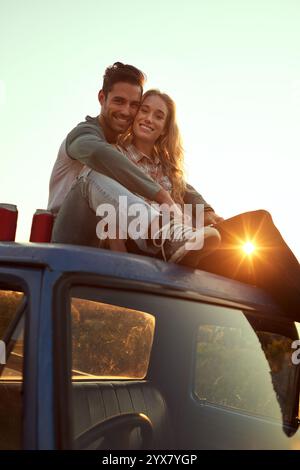 Happy couple, portrait and relax with sunset on car for road trip, holiday or vacation together in nature. Man, woman or lovers with smile or hug on Stock Photo