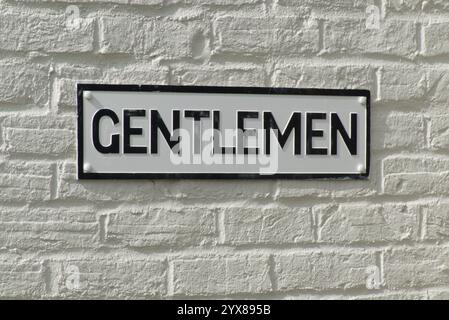 Sign at entrance to Gentlemen's toilet. Black lettering on white background on whitewashed brick wall. Stock Photo