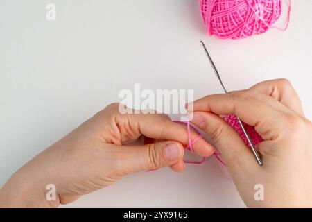 Hand holding thread of pink yarn and a chrocket hook on light background. Tutorial on how to crochet magic ring, step 2 Stock Photo