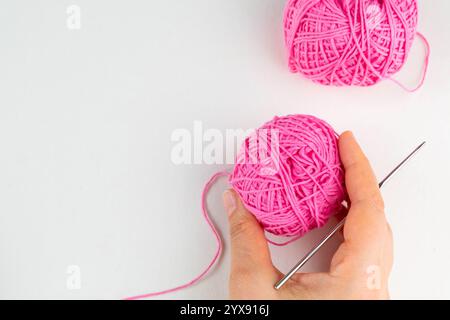 Hand holding ball of pink yarn and a chrocket hook on light background, top view Stock Photo