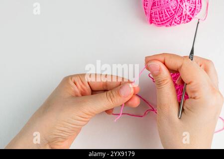 Hand holding thread of pink yarn and a chrocket hook on light background. Tutorial on how to crochet magic ring, step 1 Stock Photo