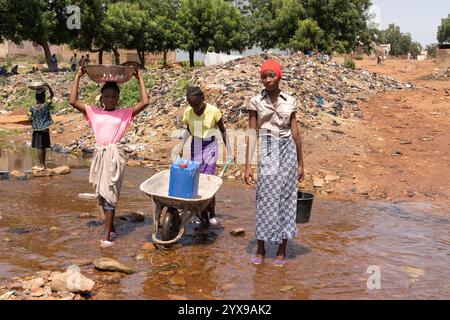 Group of African children transporting water supplies from the public well to their homes; lack of primary hydric infrastructure in developing countri Stock Photo