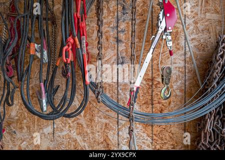 Electrical cables, chains, and a metal hook are hanging on a wall in a barn Stock Photo