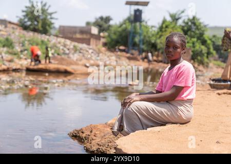 Young African girl sits lost on the edge of a flooded piece of land where her house had stood before the flood Stock Photo