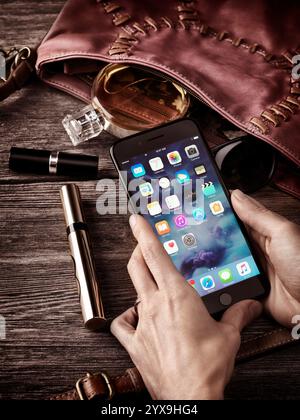 Woman hands holding Apple iPhone 7 Plus with her purse, makeup and accessories on the table conceptual still life Stock Photo