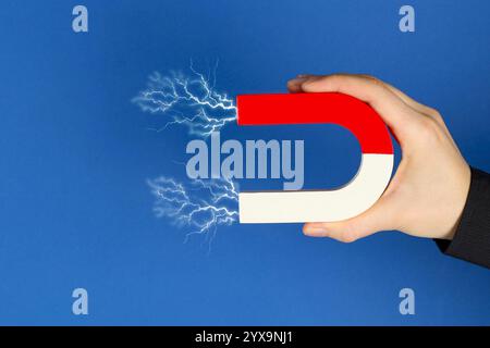 Woman holding horseshoe magnet with lightnings on blue background, closeup Stock Photo