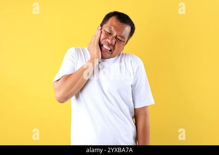 Portrait of  Asian Man Wearing White T Shirt Touching His Cheek, Has Toothache Painful Expression. Dental Problem Concept Stock Photo