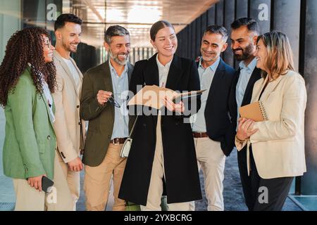 Group of diverse business people and professionals smiling and discussing ideas during a meeting, holding documents, wearing formal attire, standing together in a office building corridor. High quality photo Stock Photo