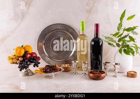 A beautiful still life for the Tu Bi shvat holiday with two bottles of white and red wine, dried fruits, nuts, fresh fruit in a vase. marble table Stock Photo