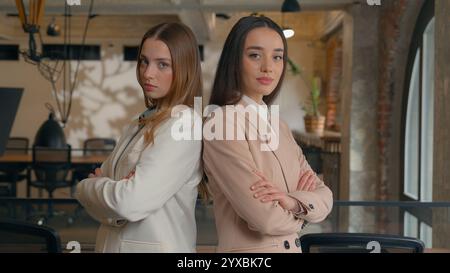 Two serious Caucasian businesswomen girls female business women partners friends coworkers colleagues managers executives posing in office crossed Stock Photo