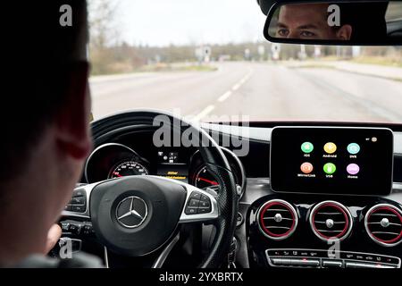 Bavaria, Germany - December 14, 2024: A young man sits at the wheel of a car while driving on a road. The interior shows a modern dashboard with integrated display and multimedia functions as well as Carplay and Android Auto *** Ein junger Mann sitzt am Steuer eines Autos, während er auf einer Straße fährt. Der Innenraum zeigt ein modernes Dashboard mit integriertem Display und Multimedia-Funktionen sowie Carplay und Android Auto Stock Photo